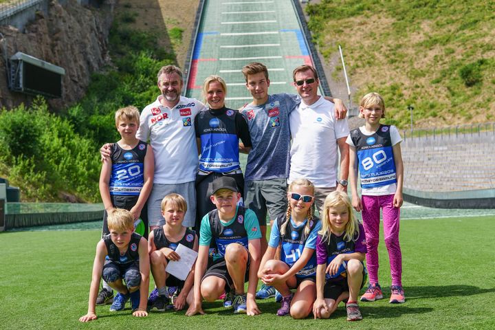 Sportssjef, Clas Brede Bråthen, Maren Lundby, Johan Forfang, markedssjef Rolf-Gunnar Solhaug omgitt av gutter og jenter på hopp camp.