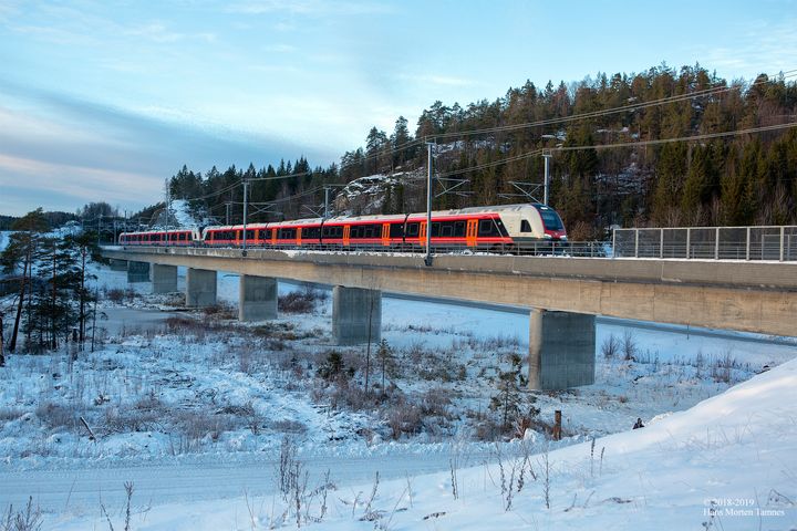 Tog kjører over jernbanebru i snøkledd landskap