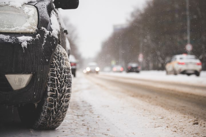 Et piggdekk fra en parkert bil står langs en trafikkerte og delvis snødekket vei.