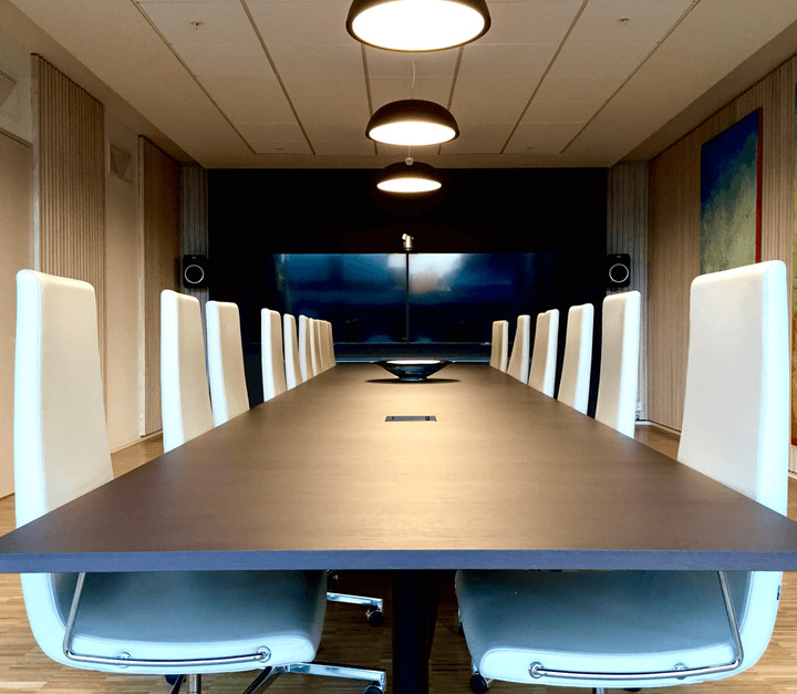 Bilde fra et møterom med langt bord og stoler med høye rygger.