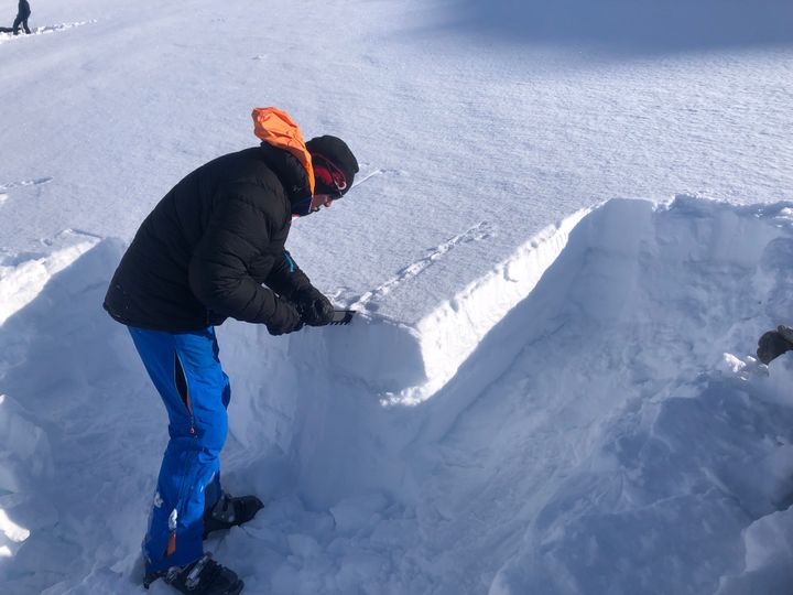 Mann står ved siden av en snøskavel og måler av snølagene.