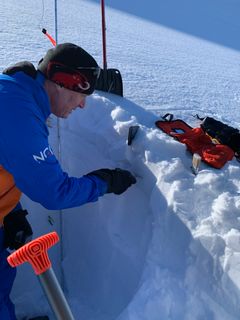 En mann står ved siden av en snøskavel og måler stabiliteten i snølagene.