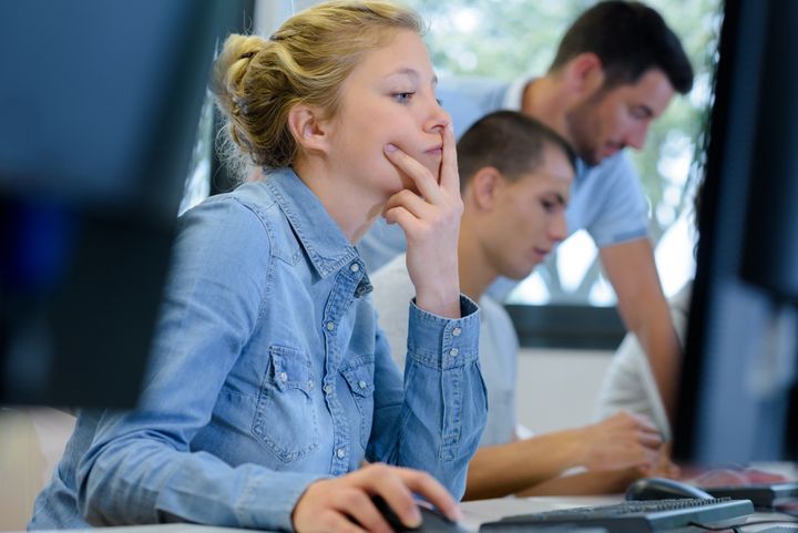 Kvinne i skjorte sitter å ser på dataskjerm. Hun har ene hånden opp mot ansiktet og ser tankefull ut.